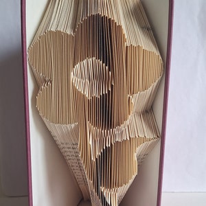 May include: A book with pages folded into a 3D design of a flower. The book is bound in a burgundy fabric cover and has a pink ribbon tied around it.