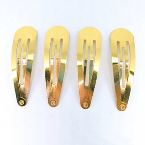 Puede incluir: Cuatro pinzas para el pelo de metal dorado con un diseño sencillo. Cada pinza tiene tres líneas paralelas cortadas en el metal.