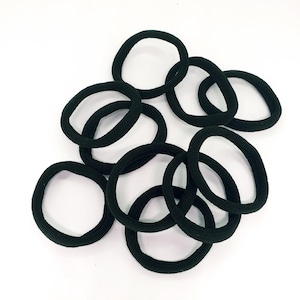 Può includere: Un mucchio di elastici per capelli neri, noti anche come scrunchies, realizzati in tessuto. Gli elastici sono di varie dimensioni e sono tutti a fuoco.