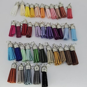 Puede incluir: Una colección de borlas de gamuza de colores con tapas y cierres de metal plateado. Las borlas están disponibles en varios colores, incluyendo blanco, amarillo, naranja, rosa, rojo, morado, azul, verde y marrón. Ideales para la fabricación de joyas o proyectos de artesanía.