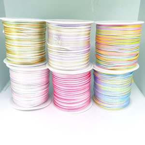 May include: Six spools of colourful embroidery floss, each wound around a white plastic spool. The floss colours include pastel pink, yellow, blue, green, purple, and white.