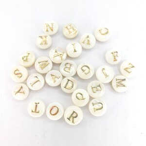 May include: White round beads with gold letters of the alphabet. Each bead has a different letter.