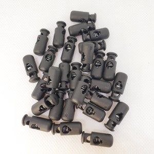 May include: A close-up of a pile of black plastic toggle clasps. The clasps are used for securing cords, straps, or other items.