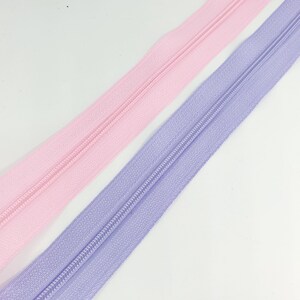 May include: Two zipper tapes, one pink and one lavender, are laid out side by side. The zippers are closed and the tape is visible.