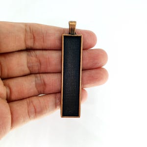 May include: A copper-toned metal pendant with a rectangular glass insert. The pendant has a loop at the top for attaching a chain.