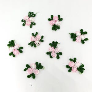May include: Nine pink and white flower appliques with green leaves. The appliques are made of fabric and have a delicate, embroidered look.