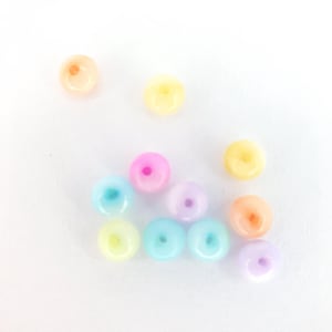 May include: Assortment of pastel coloured plastic beads. The beads are round with a hole in the centre. The colours include light blue, light pink, light yellow, and light purple.