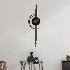 Op de afbeelding: Een moderne zwarte wandklok met goudkleurige wijzers en een ronde wijzerplaat. De klok heeft een uniek ontwerp met verticale en gebogen lijnen en een kleine slinger. De klok is aan een witte muur bevestigd.