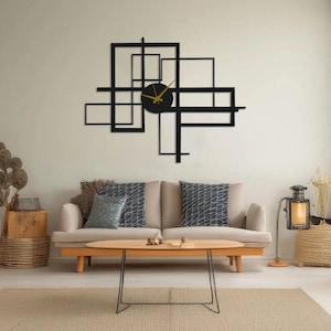 Puede incluir: Un reloj de pared geométrico negro con manecillas doradas. El reloj presenta una esfera circular y está rodeado de formas rectangulares negras. Está montado en una pared clara sobre un sofá beige.