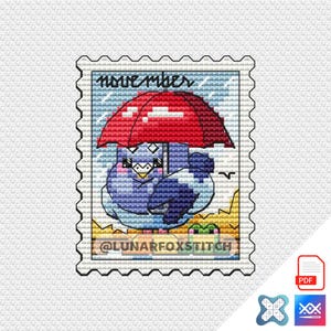 May include: A cross-stitch design featuring a blue bird under a red umbrella, with the word "november" at the top. The design is on a postage stamp-like background, with the text "@LUNARFOXSTITCH" at the bottom.