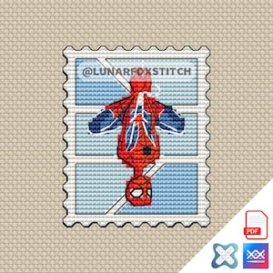 Pode incluir: Um padrão de ponto cruz com design de selo postal apresentando uma figura de super-herói vermelha e azul pendurada de cabeça para baixo. O design inclui o texto @LUNARFOXSTITCH em letras pretas sobre um fundo azul claro com linhas de grade brancas.