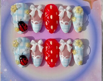 May include: Set of ten false nails with a blue and white gingham pattern, red and white polka dot pattern, white bows, and ladybug accents.