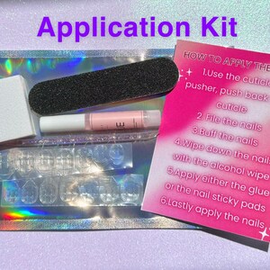 May include: A pink and white instruction card with steps on how to apply press-on nails. The card is next to a clear plastic bag with a nail file, cuticle pusher, glue, and nail adhesive tabs.