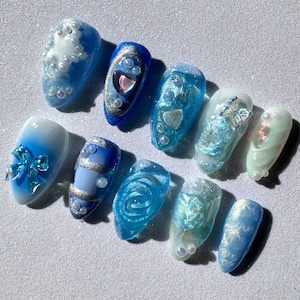 May include: A set of ten blue and white nail art designs. The designs include a heart, a bow, a flower, a butterfly, and a swirl. The designs are all different sizes and shapes.
