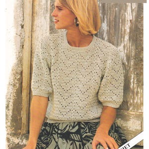 Peut inclure: Une femme portant un pull en crochet cr&egrave;me avec un motif ajour&eacute;. Le pull a des manches courtes et un col rond. La femme est assise sur un banc en bois avec une jupe &agrave; motifs. Le texte sur l'image est "4 Ply Cotton 28 to 38/40 ins CROCHET".