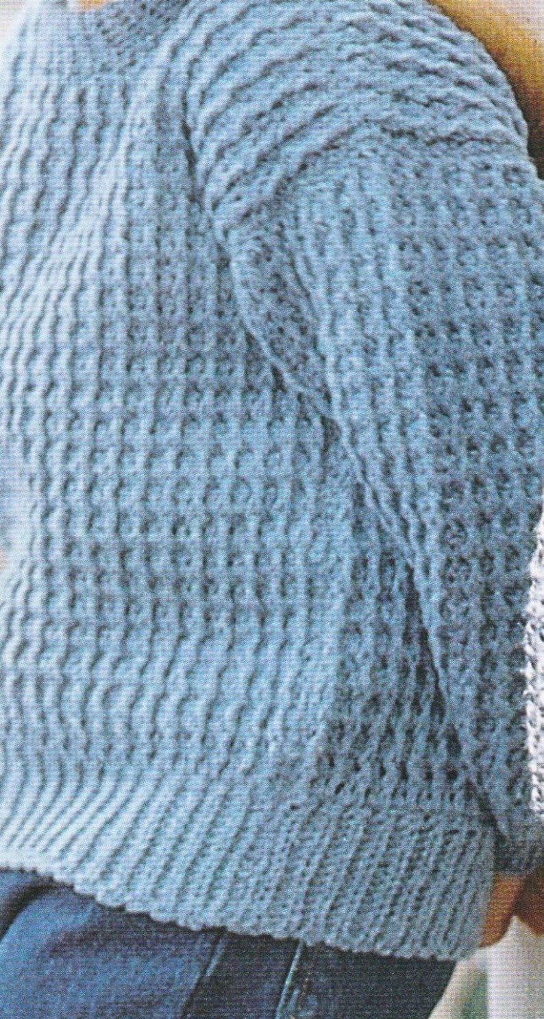 Puede incluir: Un su&eacute;ter de punto azul claro con un patr&oacute;n texturizado. El su&eacute;ter se muestra desde la parte posterior y las mangas son visibles.