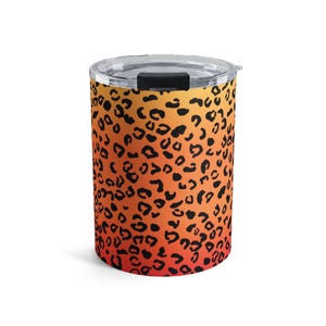 May include: A cylindrical travel mug with a clear lid and a black sliding closure. The mug features a vibrant leopard print design in shades of orange and black. The mug is designed to keep beverages hot or cold.