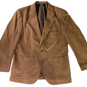 May include: A brown blazer with a two-button closure, two front pockets, and a notched lapel. The jacket has a classic design and is made of a soft, suede-like material. The blazer is a medium brown color.