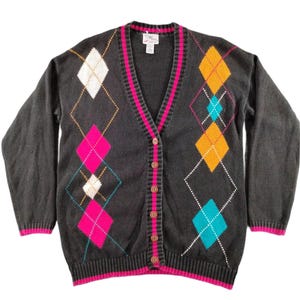 Könnte beinhalten: Eine anthrazitfarbene Strickjacke mit V-Ausschnitt und einem lebendigen Argyle-Muster in den Farben Pink, leuchtendem Orange, Weiß und Türkis. Das Kleidungsstück verfügt über eine Knopfleiste, gerippte Bündchen und einen gerippten Saum mit pinkfarbenen Details.