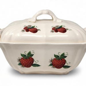May include: A cream-colored ceramic tureen with a matching lid and two side handles. The exterior features a repeating pattern of red strawberries with green leaves and small white flowers on both the main body and the lid.