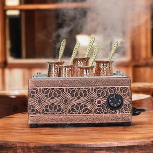 Könnte beinhalten: Eine kupferfarbene elektrische Kaffeemaschine mit dekorativem Design. Sie verfügt über sechs einzelne Kaffeekannen aus Kupfer mit Griffen und einem Temperaturregler. Dampf steigt aus den Kannen auf.