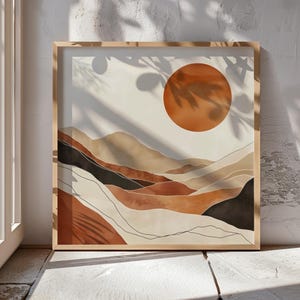 Peut inclure: Une impression d'art murale carrée dans un cadre en bois clair représentant un paysage abstrait avec des collines superposées dans des tons terre cuite, beige et noir. Un grand cercle orange brûlé représente le soleil dans le coin supérieur.