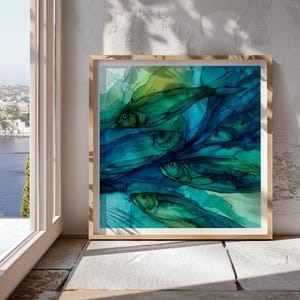 Può includere: Una stampa artistica incorniciata con un dipinto ad acquerello astratto di diversi pesci in tonalità blu e verde. L'opera d'arte ha una qualità fluida ed eterea, con i pesci che sembrano nuotare nell'acqua. La cornice è di colore legno chiaro.