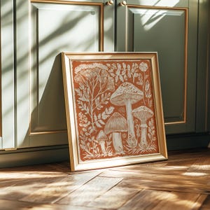 A framed illustration of mushrooms and plants is displayed on a wooden floor against a green cabinet.