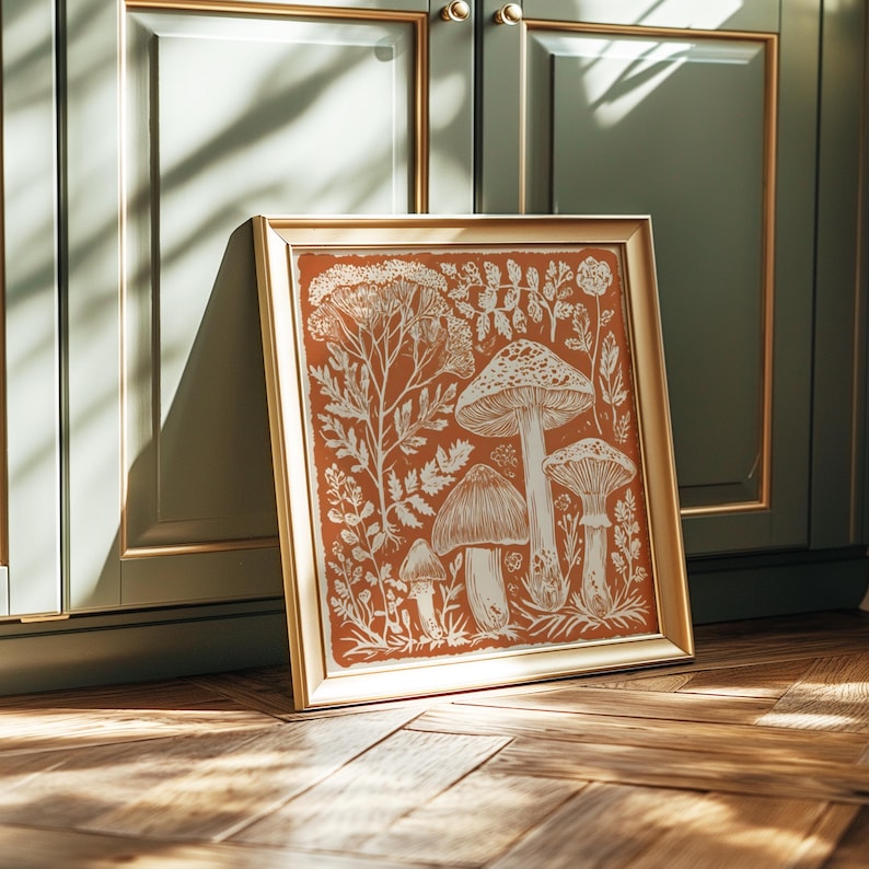 A framed illustration of mushrooms and plants is displayed on a wooden floor against a green cabinet.