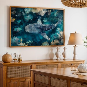 a large framed painting of a blue whale swimming in the ocean, hanging on a wall above a wooden cabinet.