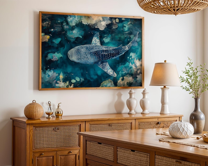 a large framed painting of a blue whale swimming in the ocean, hanging on a wall above a wooden cabinet.