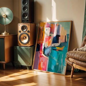 a modern living room with a large abstract painting on the wall, a brown leather chair, a wooden side table with a lamp, and a stack of speakers.