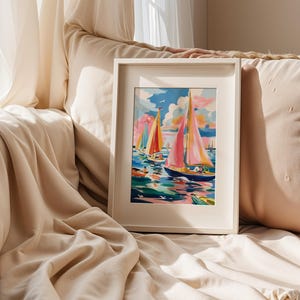 A framed painting of colorful sailboats is displayed on a beige couch, with a window and white curtains in the background.