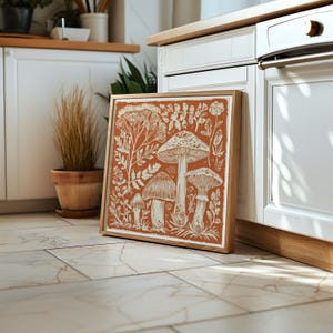 Autumn mushroom art print featuring a tall central mushroom surrounded by smaller mushrooms and woodland botanicals in warm earthy tones. Detailed fall botanical illustration that captures the beauty of forest landscapes, ideal for rustic kitchens, autumn cottagecore interiors, woodland décor or seasonal gallery walls. Perfect mushroom wall art for adding warm autumn charm and woodland character to any space.