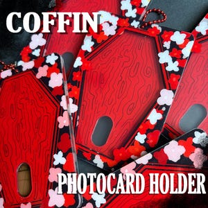 Pode incluir: Porta-cartões fotográficos vermelhos em forma de caixão com um design de grão de madeira. Os porta-cartões são decorados com um padrão floral em vermelho, branco e rosa. A palavra "COFFIN" é impressa no topo e "PHOTOCARD HOLDER" na parte inferior.