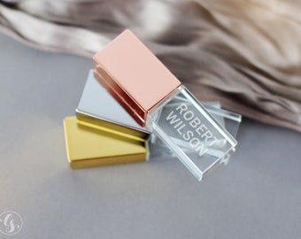 May include: A stack of three rectangular USB flash drives with metallic caps in rose gold, silver, and gold. The clear acrylic body of the top drive features the engraved white text ROBERT WILSON, showcasing a sleek, modern design for data storage.