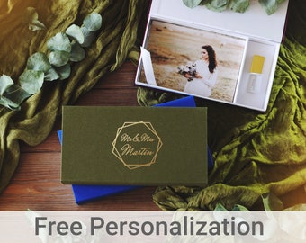 May include: A green box with a gold inscription that reads "Mr. & Mrs. Martin" on a wooden surface with green fabric and a white box containing a photo and a USB drive.