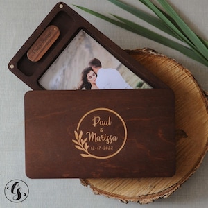May include: A wooden keepsake box with a photo and a USB drive. The box is engraved with the names "Paul & Marissa" and the date "12-17-2022". The box is open, revealing a photograph of a couple. The USB drive is also engraved with the names and date.