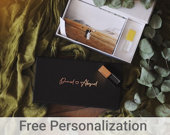May include: A black box with a gold inscription that reads "Daniel ♥ Abigail" and a gold USB drive. The box is on a green fabric surface with a white box containing a photo and a yellow USB drive.