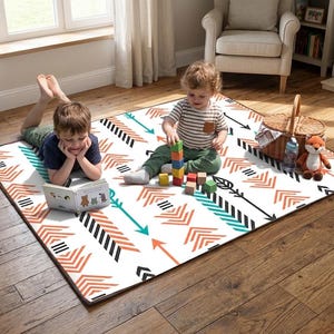 Puede incluir: Alfombra de juego rectangular con fondo blanco y un patrón de flechas en negro, turquesa y naranja. Dos niños juegan en la alfombra, uno leyendo un libro y el otro con bloques de madera. Una cesta y un zorro de peluche también están presentes.