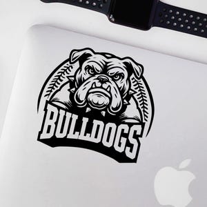May include: Black and white illustration of a bulldog with a fierce expression. The bulldog is wearing a spiked collar and is surrounded by a baseball-themed design. The text "BULLDOGS" is written in a bold, stylized font below the bulldog.