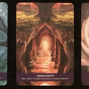 May include: Three tarot cards with colorful imagery. The first card shows a blue and white figure with a bird head. The second card shows a stone archway with a light at the end of the path. The third card shows a purple circle with a geometric pattern inside. The text on the cards reads "Thoth Light Codes", "Inner Earth", and "The Divine Matrix".