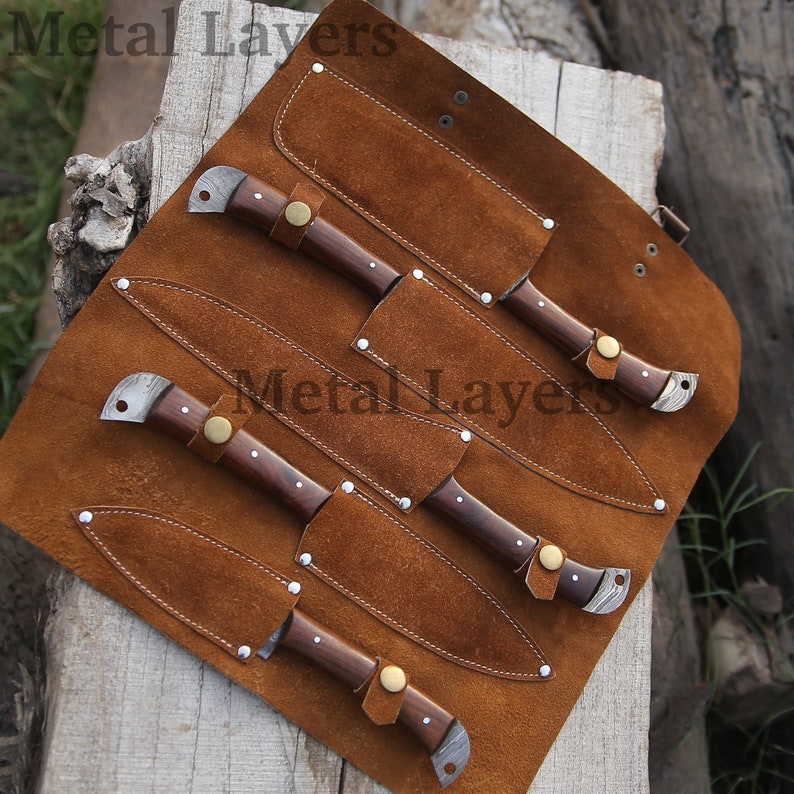 May include: A set of five knives with wooden handles and leather sheaths, rolled up in a brown leather carrying case. The case has the text "Metal Layers" printed on it.