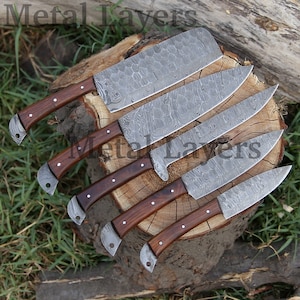 May include: Set of six kitchen knives with wooden handles. The blades are made of Damascus steel and have a distinctive pattern. The knives are arranged on a wooden surface.