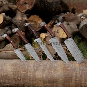 May include: Set of six kitchen knives with wooden handles and patterned blades. The knives are arranged on a wooden log.