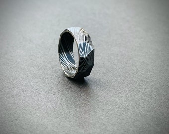 May include: A black and white patterned metal ring with a faceted design.