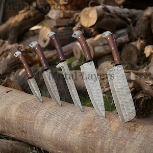 May include: Set of six kitchen knives with wooden handles and patterned metal blades. The knives are arranged on a wooden log.