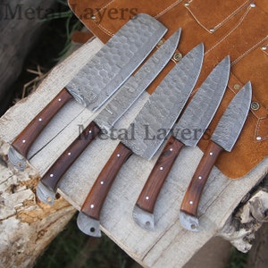 May include: Set of six kitchen knives with wooden handles. The knives have a Damascus steel blade pattern and are arranged on a wooden surface.
