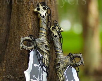 May include: Two ornate swords with black blades and gold-colored handles are connected by a black chain. The swords have intricate designs and skulls on the handles.