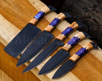 May include: Five black kitchen knives with wooden handles featuring a purple and brown marbled design. The knives are arranged on a wooden surface.